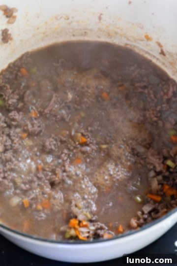 Using a slotted spoon to transfer browned ground beef from the Dutch oven into a large mixing bowl, leaving the sauce base behind.
