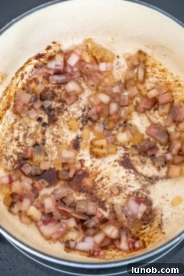 Pancetta frying gently in a Dutch oven, rendering its fat.