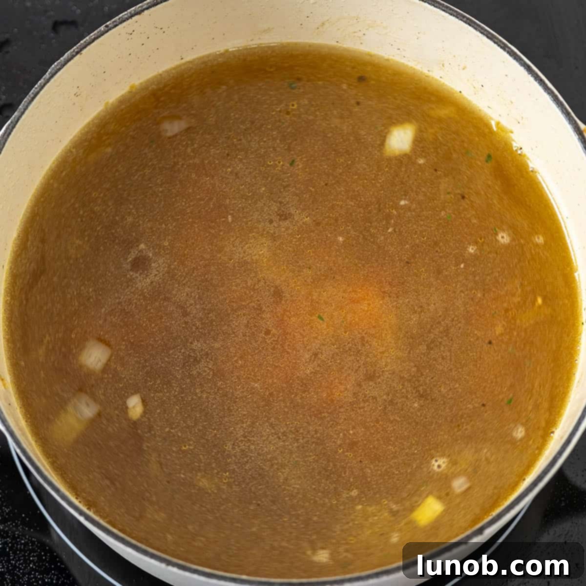 Rustic Italian Meatball & Escarole Soup 6 Chicken broth being poured into a pot with sautéed vegetables (onions, carrots, garlic).