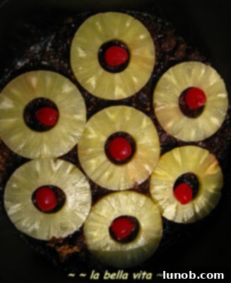A warm Pineapple Upside-Down Cake cooling in a cast iron skillet, with bubbly caramel around the edges.