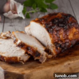 Close-up of a perfectly roasted pork loin with a rich, golden crust, garnished with fresh thyme and garlic cloves, ready to be sliced and served.