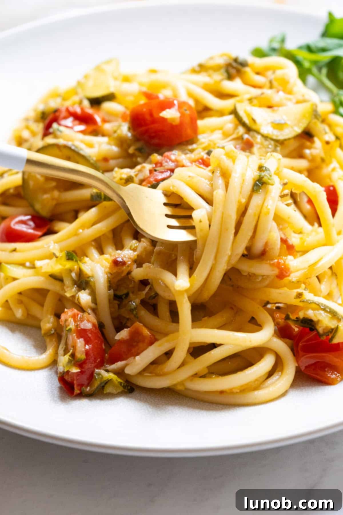 Close-up of Italian Summer Zucchini Pasta with cherry tomatoes being lifted by a fork, showcasing the creamy, vibrant sauce.