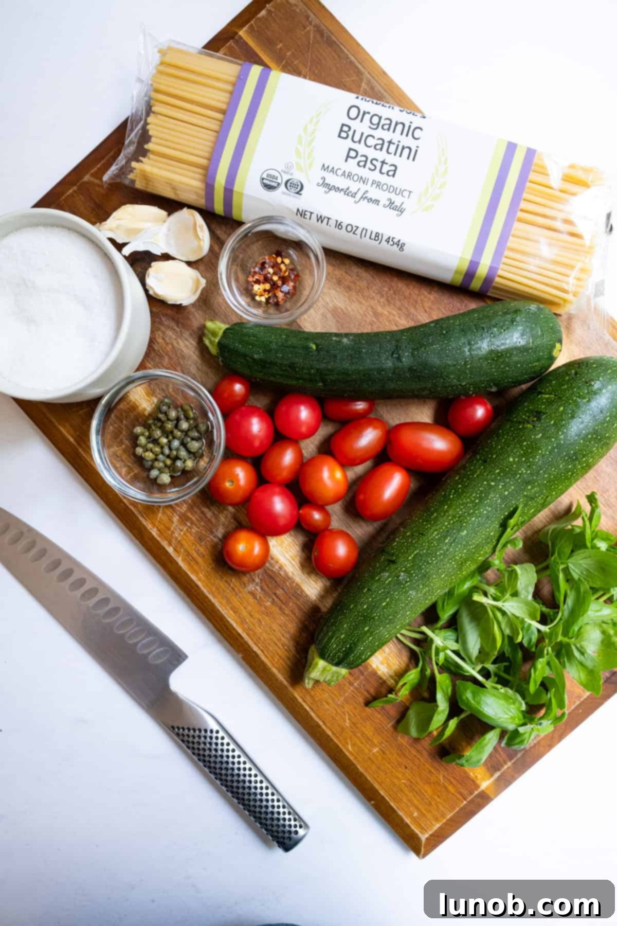 Ingredients laid out for the Italian Summer Zucchini Pasta dish, including fresh zucchini, cherry tomatoes, garlic, and bucatini pasta.
