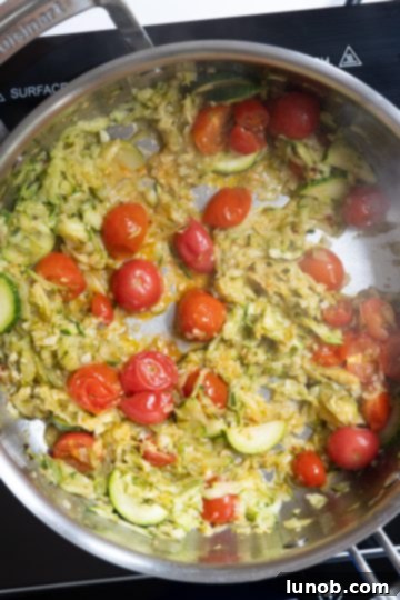 The zucchini and cherry tomato sauce beginning to break down and simmer in the pan, releasing juices and softening.