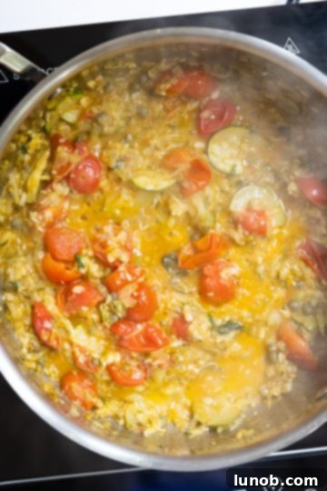 The pasta sauce, now with capers and basil, beginning to redden and thicken, indicating it's almost ready.