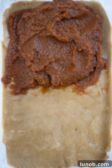 blondie dough spread out with pumpkin butter on top, ready for final layer