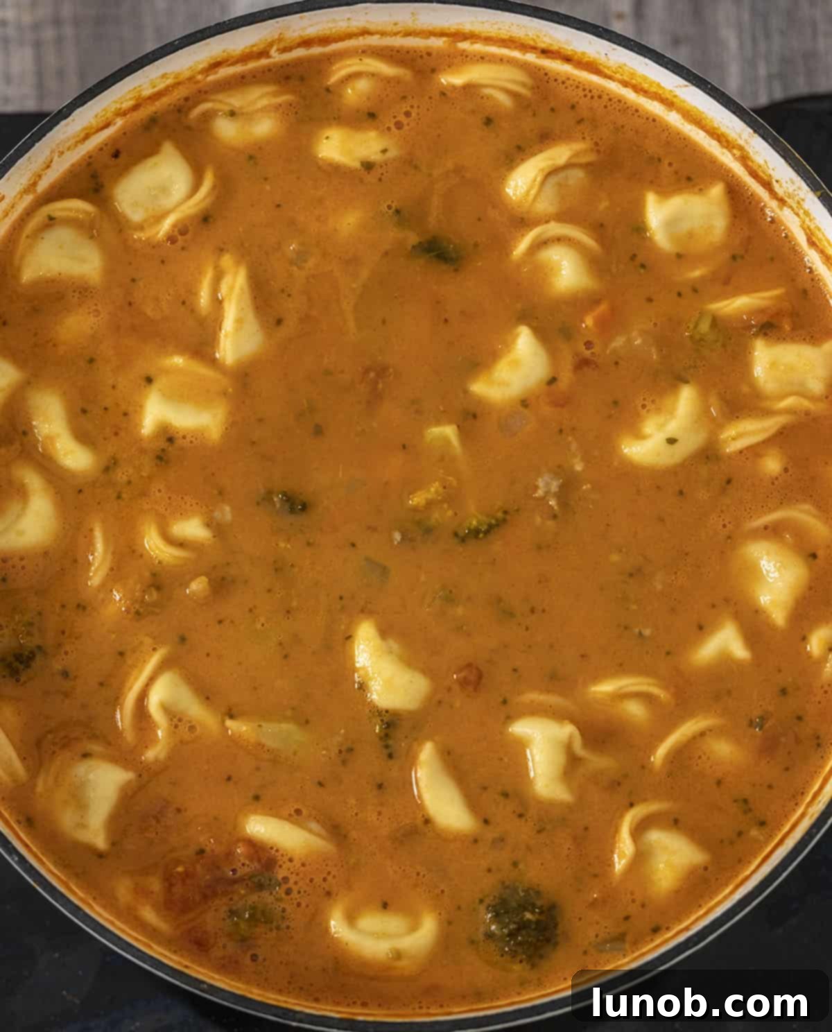 Heavy cream being stirred into the Rustic Italian Tortellini Soup, creating a creamy texture