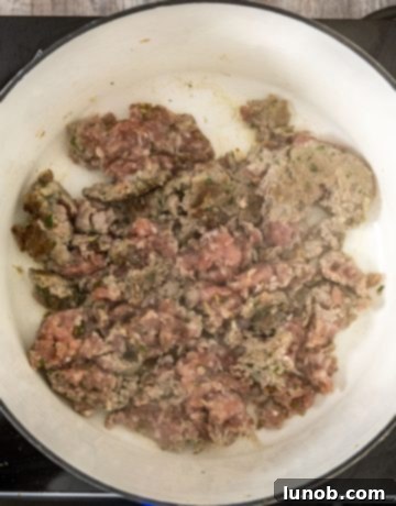 Partially browned Italian sausage being broken apart with a wooden spoon in a dutch oven