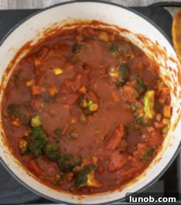 Pouring crushed tomatoes into the dutch oven with vegetables and broccoli