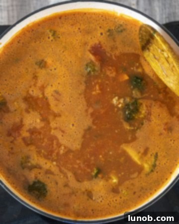 Pouring chicken broth into the simmering soup base in a dutch oven