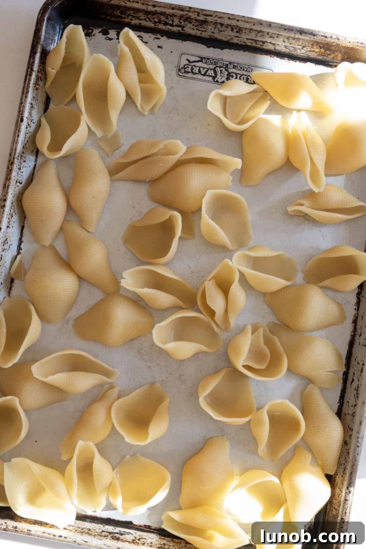 Par-cooked jumbo shells cooling on an oiled baking sheet to prevent sticking.