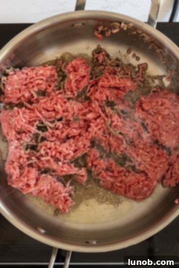 Ground beef browning in a large saucepan on the stovetop.