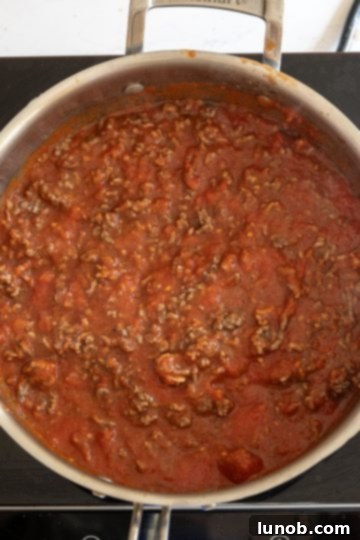 Meat sauce simmering with browned ground beef returned to the pan.