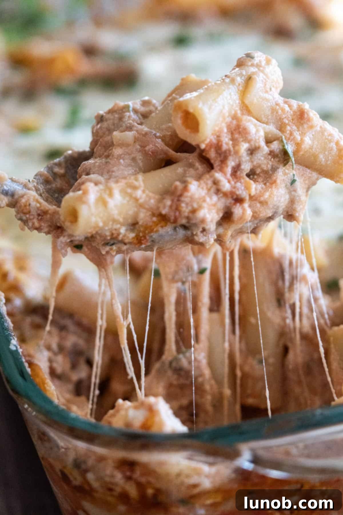 Cheesy pull of baked ziti on a spoon being scooped from the baking dish, showing gooey melted cheese