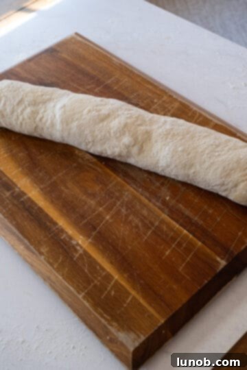 The pepperoni stromboli dough, filled with cheese and meat, is tightly rolled into a log shape