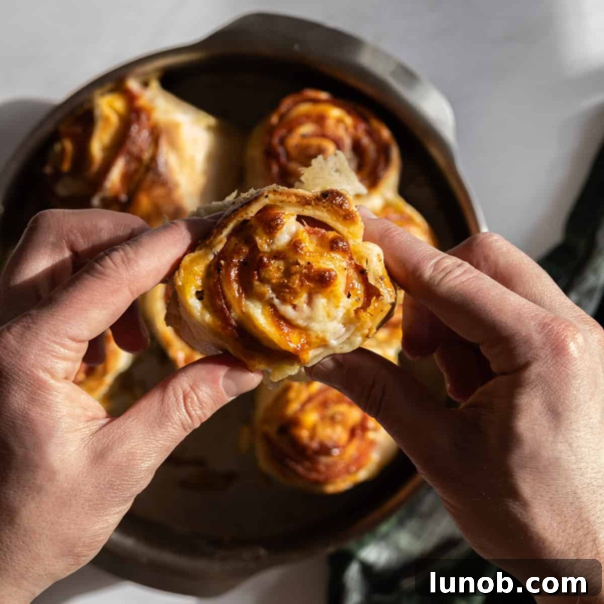 A hand holding a slice of pepperoni stromboli, showing the melted cheese and meat filling