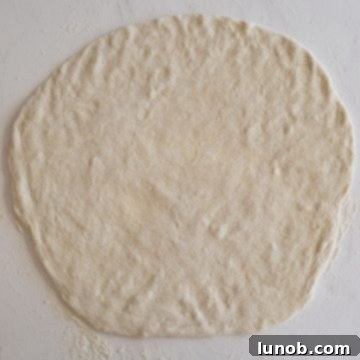 Pizza dough rolled out thinly on a heavily floured surface, forming a large rectangular shape, ready for the filling.