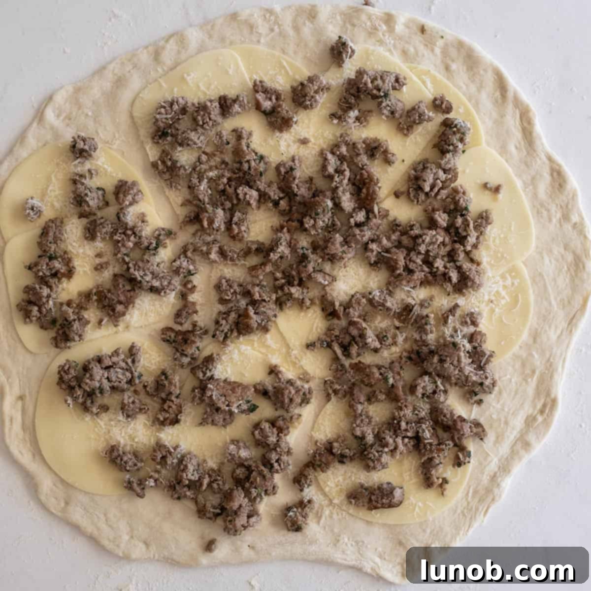 Pizza dough generously topped with cooked ground Italian sausage and a medley of cheeses, ready to be rolled into a loaf.