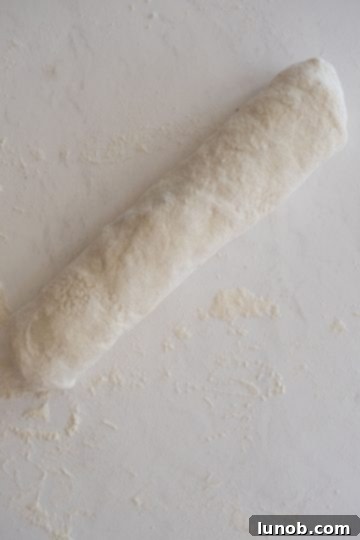 The filled dough expertly rolled into a compact bread loaf, with sealed edges, ready for egg wash and seasoning.
