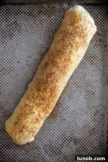 The raw bread loaf, beautifully brushed with egg wash and generously seasoned with paprika, garlic powder, salt, and pepper.