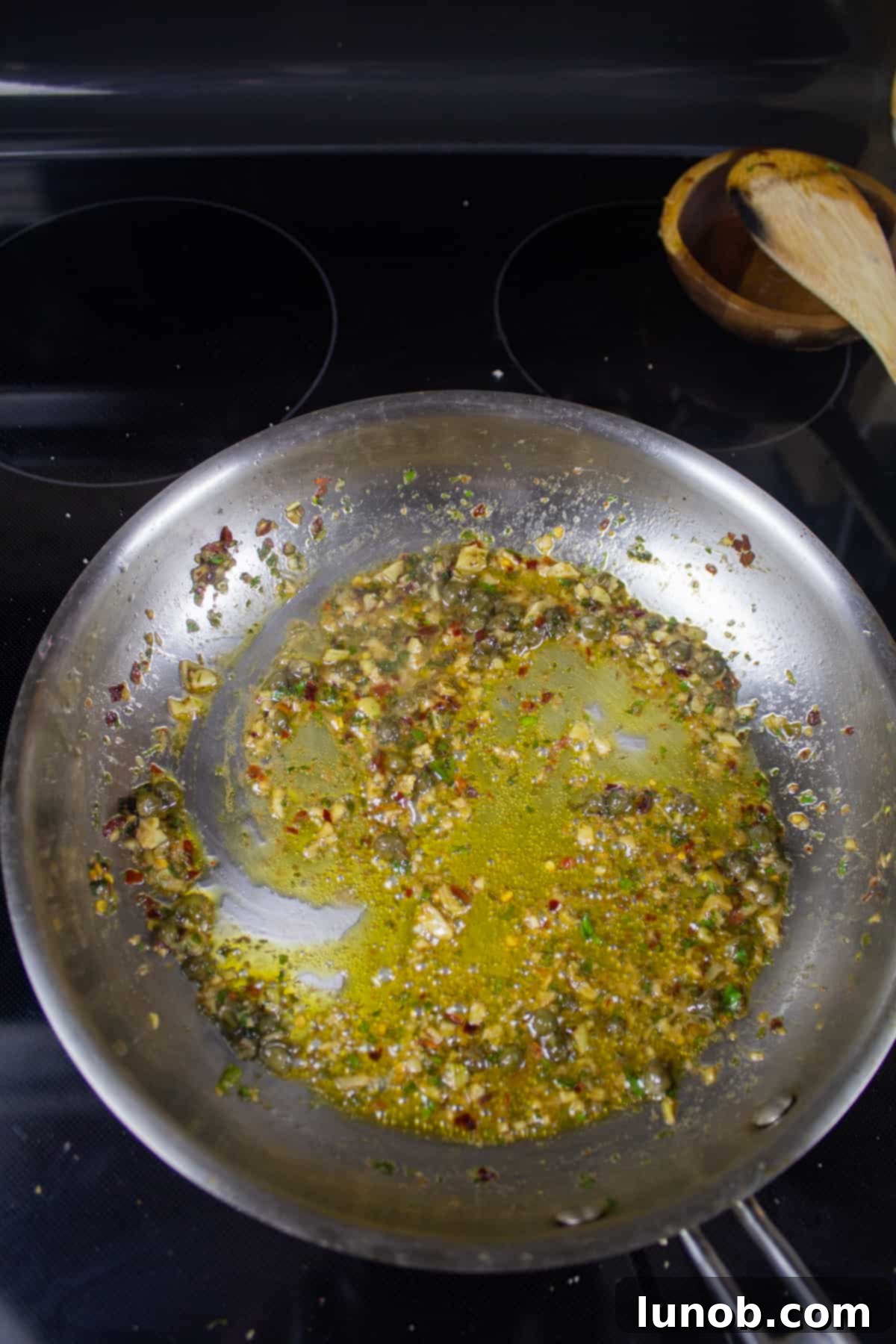 Garlic, Anchovy, capers, and parsley simmering in olive oil in a pan on the stove, forming the savory sauce base