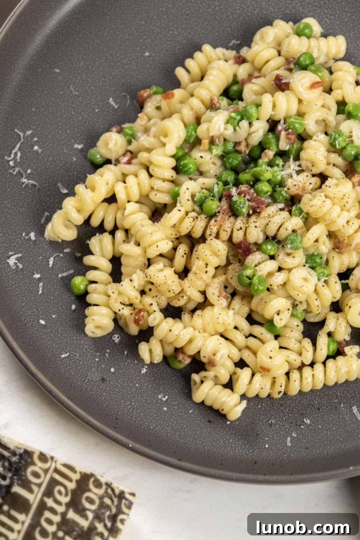 A vibrant bowl of pasta with peas and crispy pancetta, garnished with fresh herbs and grated cheese, ready to be served.