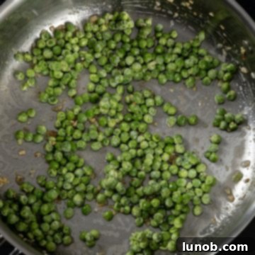 Fresh peas being added to a hot pan with garlic