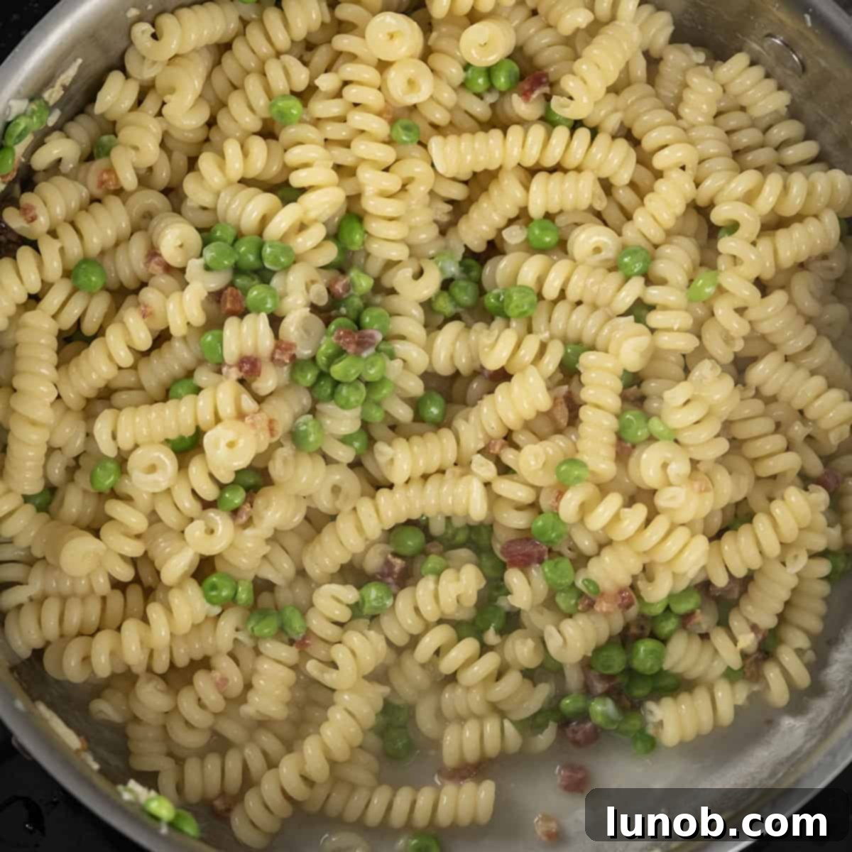 Close-up of pasta with peas being tossed in a pan, coated in sauce