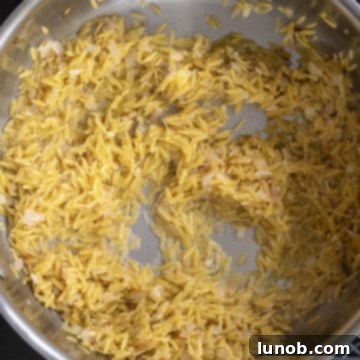 Bright Lemon Spinach Orzo 5 Orzo pasta being toasted in a pan with sautéed shallots and garlic.