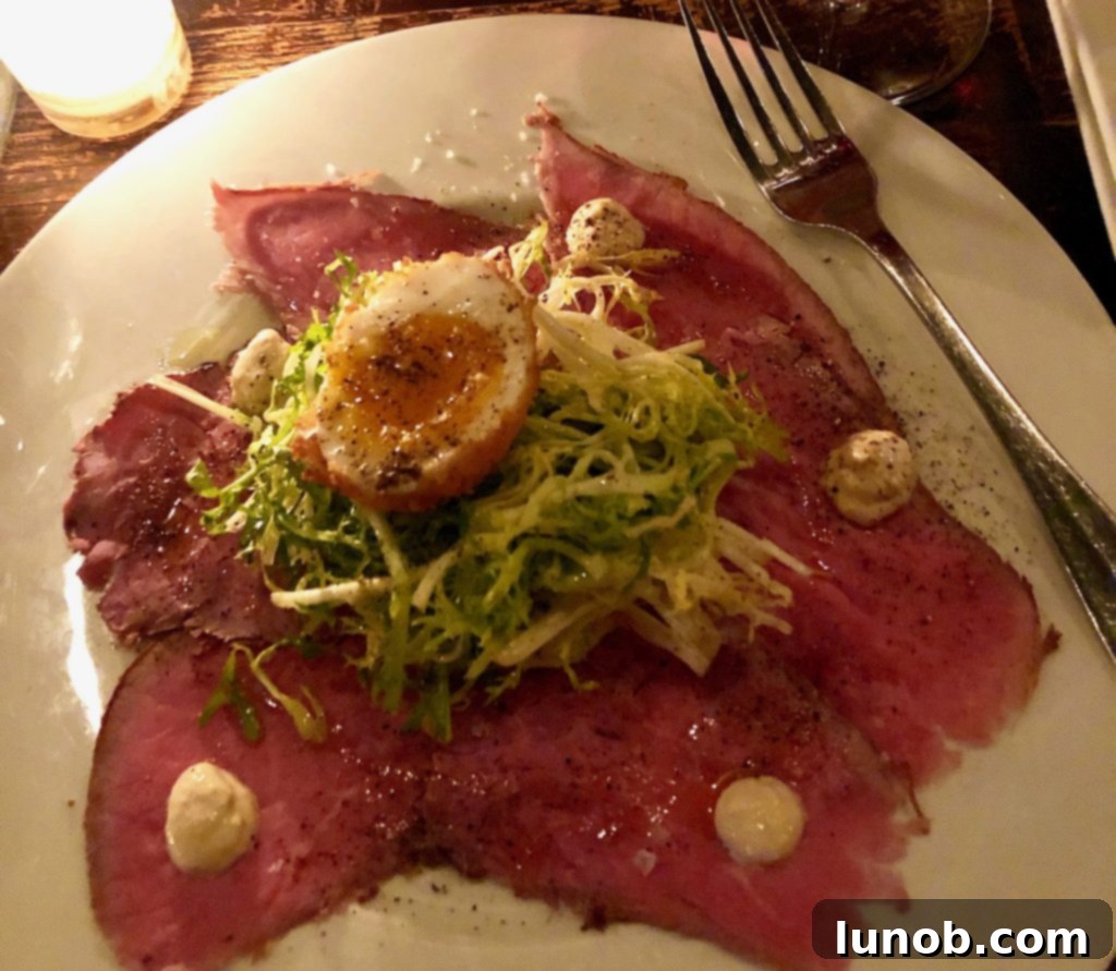 An exquisite close-up of the Filetto e Fegato dish, featuring tender beef slices alongside creamy chicken liver pate, garnished with vibrant capers and crisp crackers.