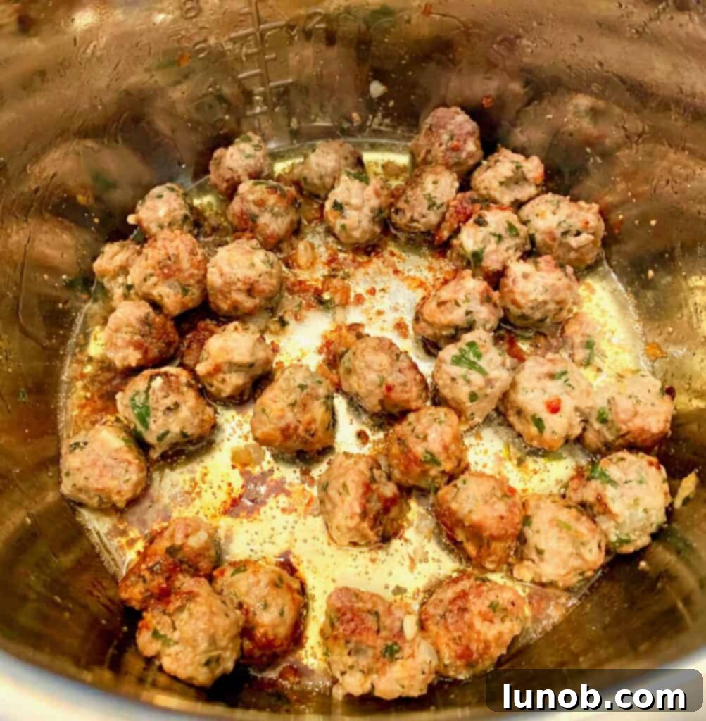 Adding chicken broth to browned meatballs in the Instant Pot for Classic Italian Wedding Soup, building the soup's foundational flavor.
