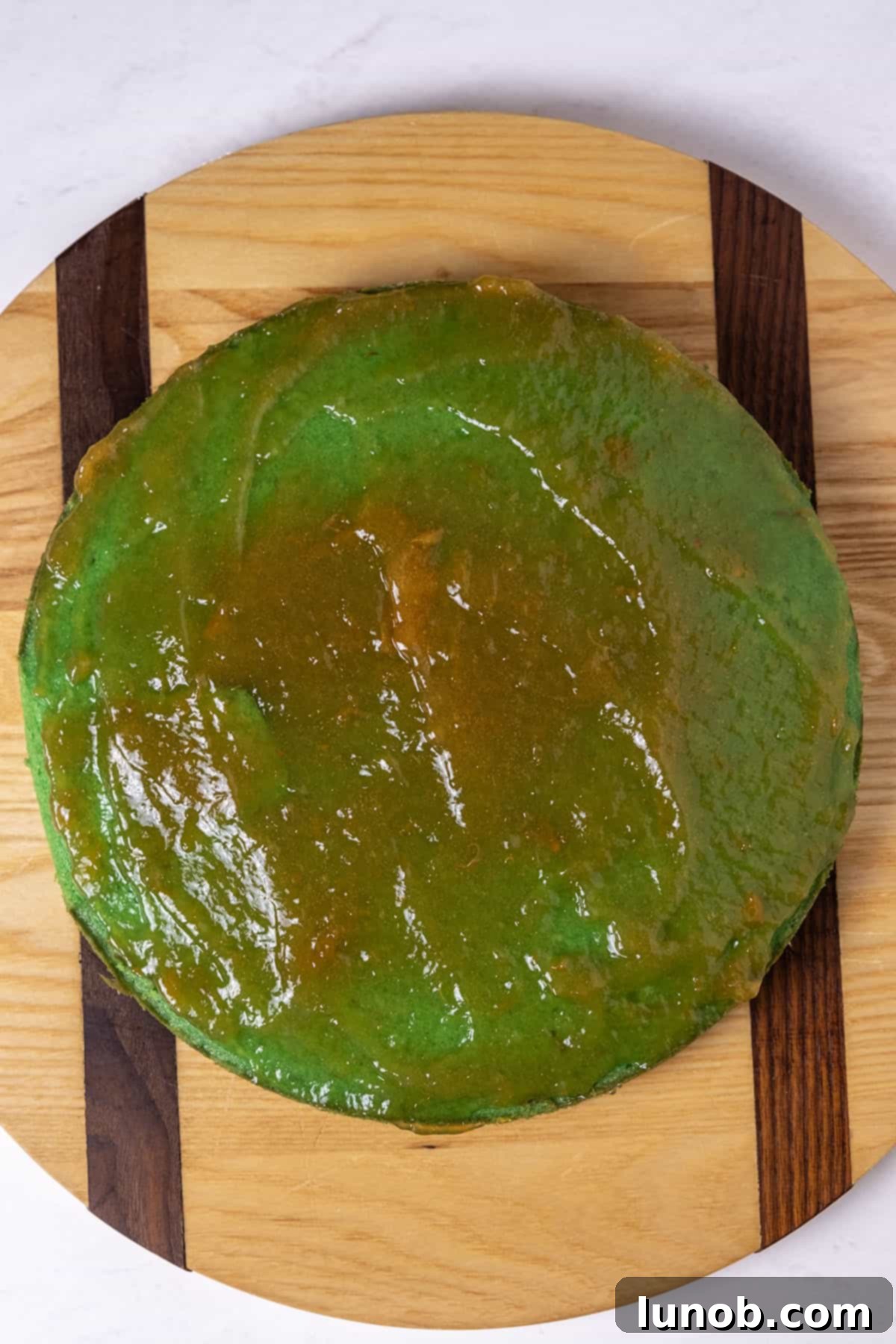 Apricot jam spread on the first green cake layer