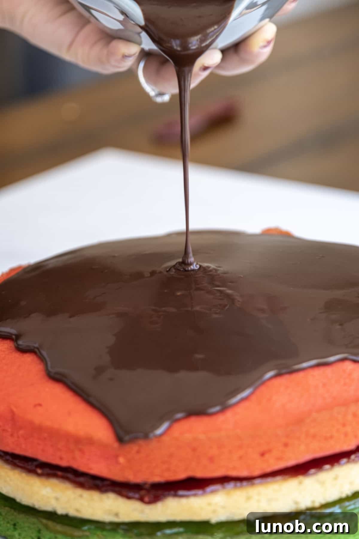 Dark chocolate ganache being spread over the entire rainbow cake