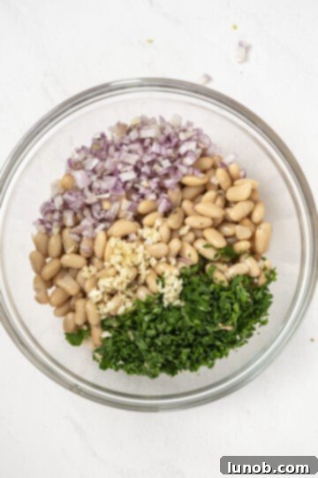 Mediterranean Farro White Bean Salad 4 A close-up shot of combined cannellini beans, finely chopped shallots, garlic, and fresh parsley in a bowl.