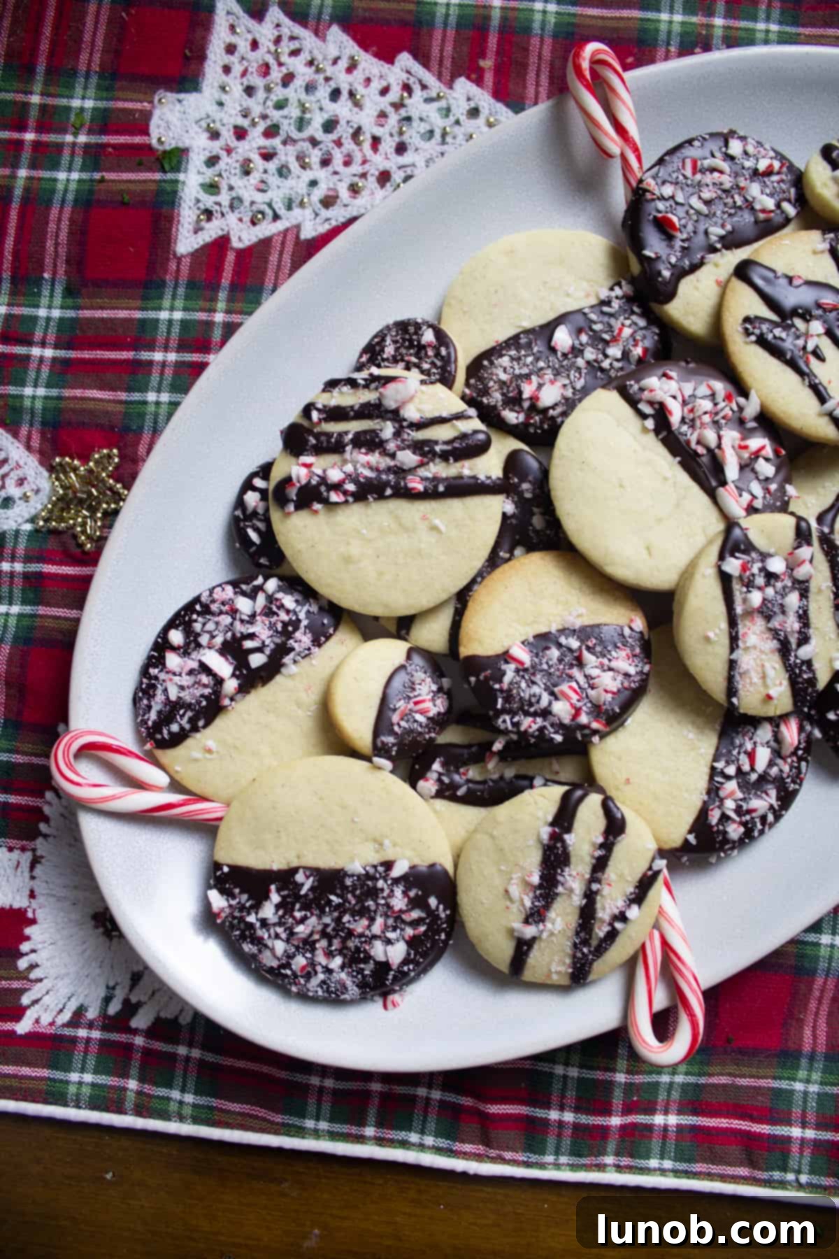 Decadent Dark Chocolate Peppermint Sugar Cookies 2 Half-dipped dark chocolate peppermint sugar cookies with candy cane crumbles on a festive plate, evoking holiday cheer.