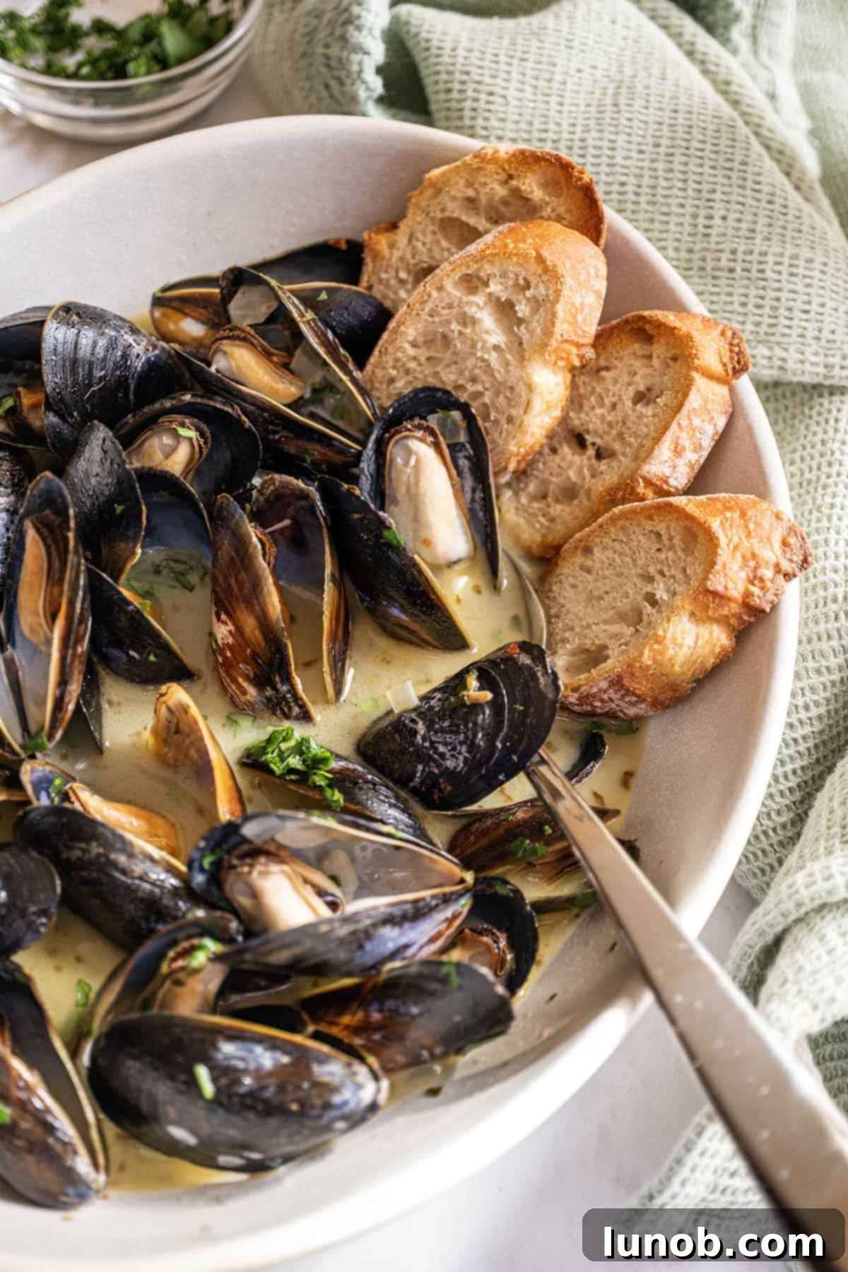 Mussels in Savory White Wine Broth 2 Steamed mussels in a serving bowl filled with white wine sauce and crostini on the side, ready to be enjoyed.