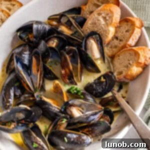 Mussels in Savory White Wine Broth 11 Steamed mussels in a serving bowl filled with white wine sauce and crostini on the side.