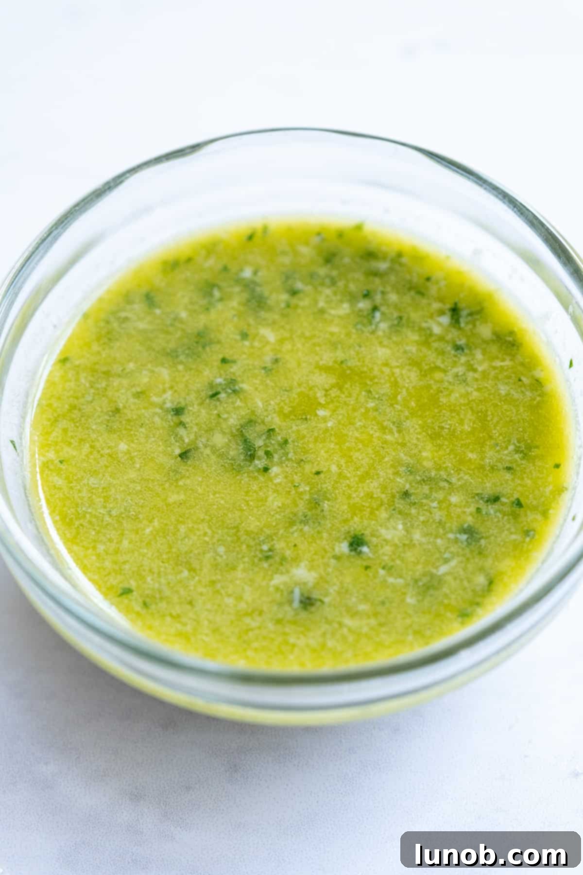 Bright green lemon basil vinaigrette in a clear glass bottle next to fresh lemons and basil leaves.