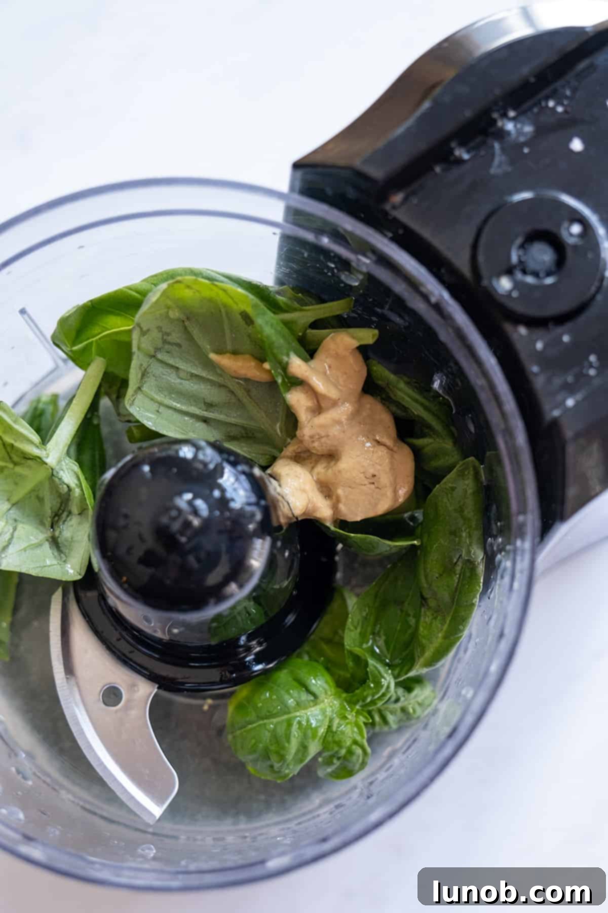 Fresh lemon basil vinaigrette ingredients being processed in a food processor, showing the vibrant green mixture.
