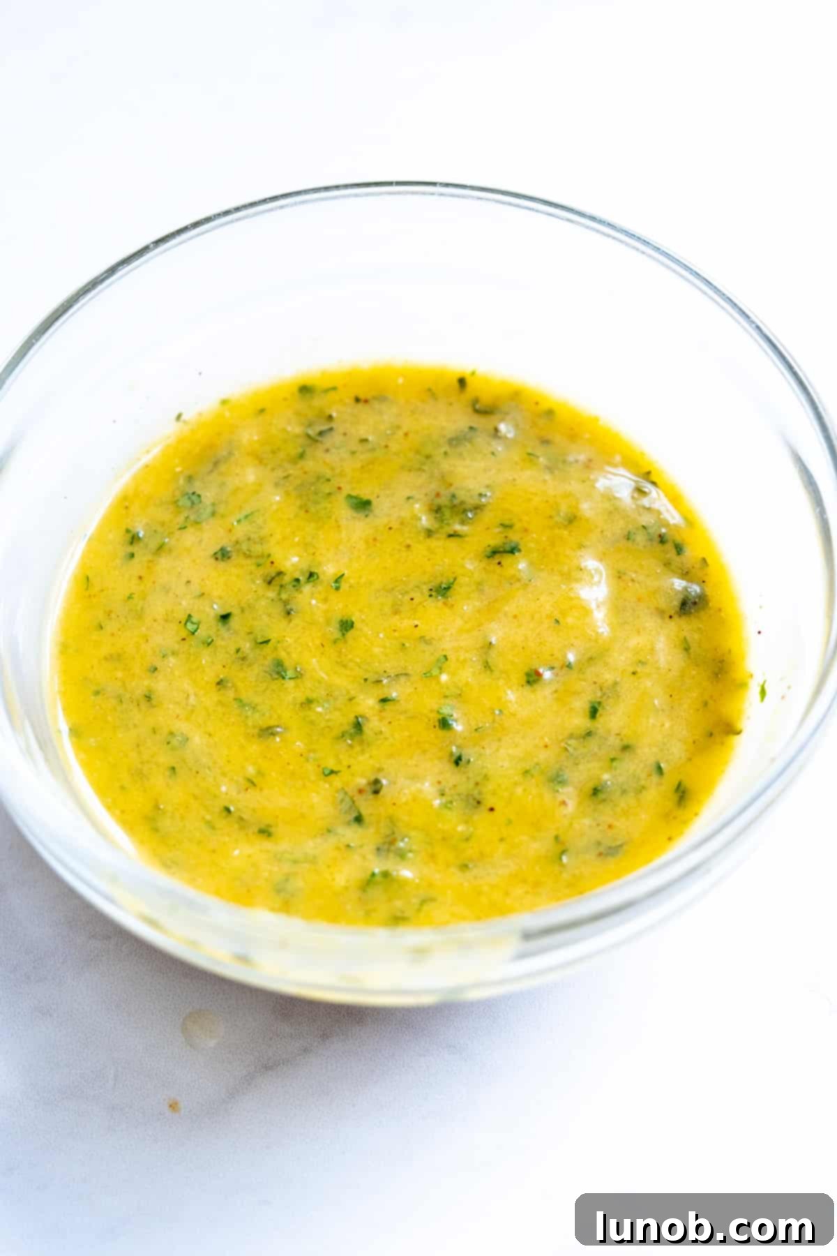 Freshly made Cilantro Mango Vinaigrette in a glass jar, vibrant yellow-green with specks of cilantro, next to a fresh mango and cilantro sprigs.