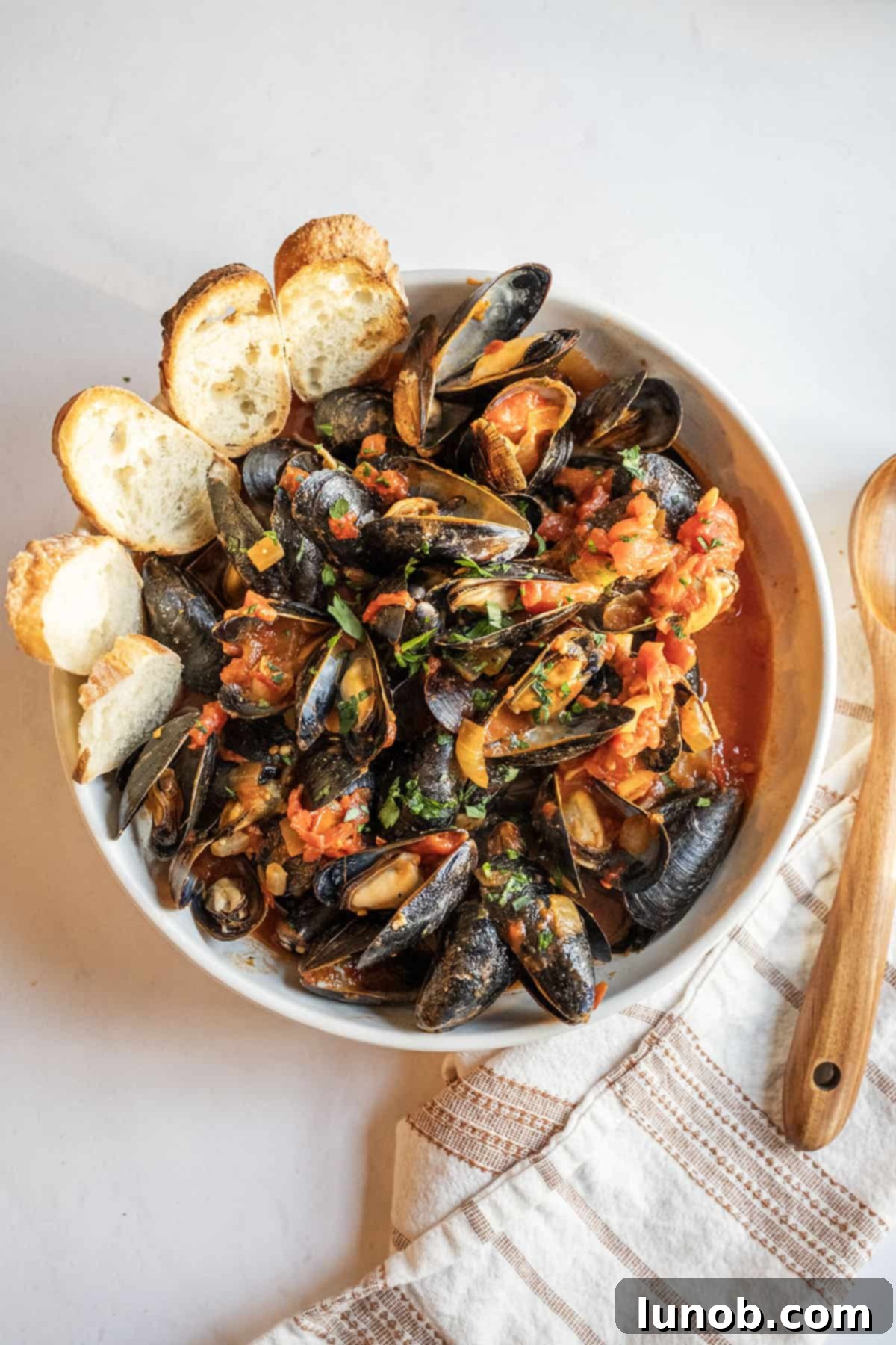 A large serving bowl filled with Mussels Fra Diavolo, garnished with fresh parsley, served alongside crusty Italian bread. 