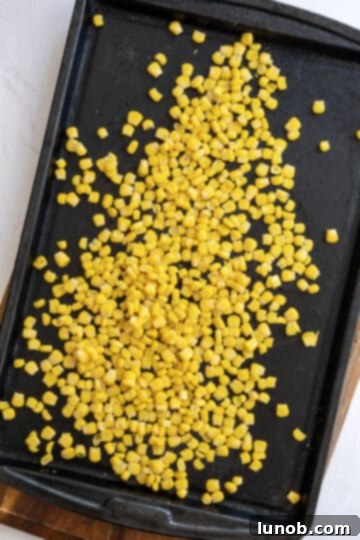 Zesty Chipotle BBQ Chicken Salad 5 Fresh corn kernels being seasoned with olive oil, salt, and pepper on a baking sheet, ready for roasting.