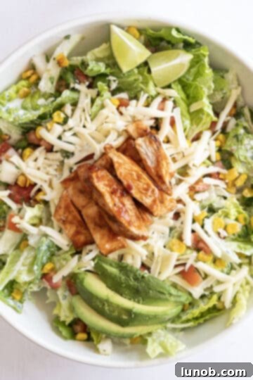 Zesty Chipotle BBQ Chicken Salad 7 Delicious sliced avocado being carefully added to a vibrant salad mix, alongside other fresh ingredients