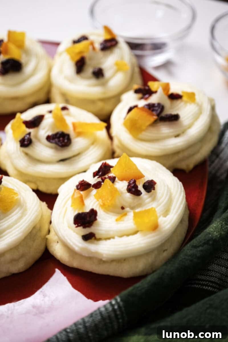 Cranberry and orange shortbread cookies topped with frosting and garnished with dried cranberries and candied oranges. These festive cookies are perfect for holiday gatherings.