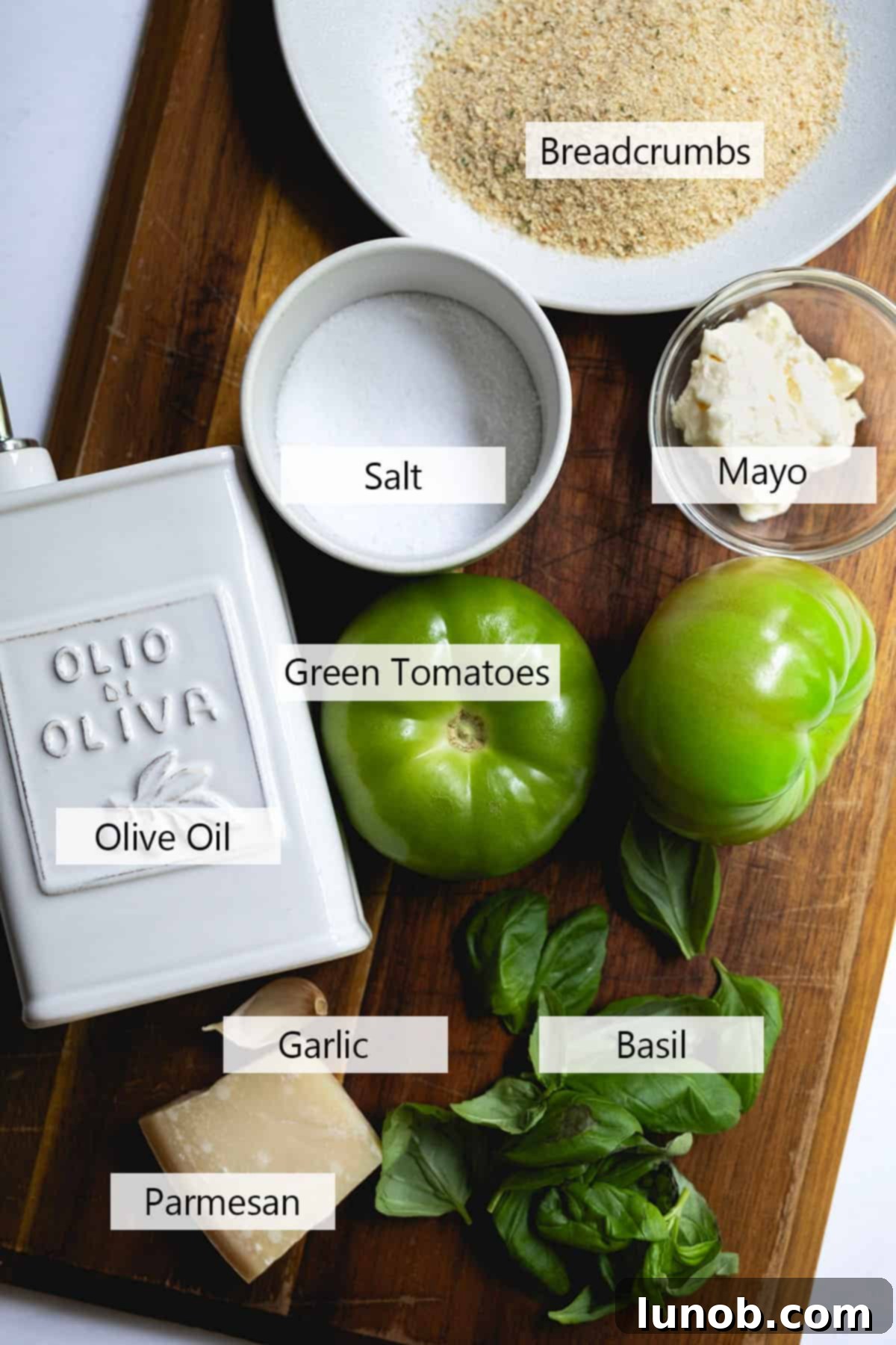 A selection of fresh ingredients including green tomatoes, basil, garlic, and cheese, laid out for the recipe.