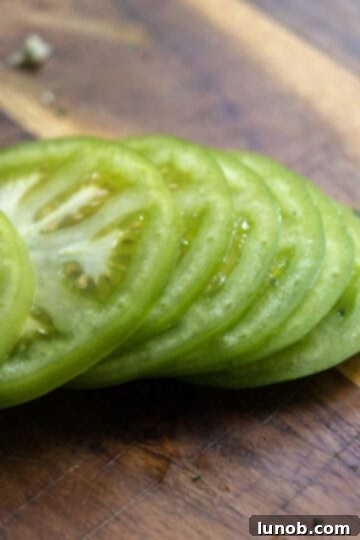 Green tomatoes uniformly sliced to a quarter-inch thickness, ready for breading.