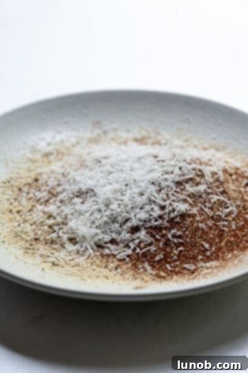 A bowl containing a dry breadcrumb mixture, seasoned with Parmesan cheese, garlic powder, salt, and paprika.