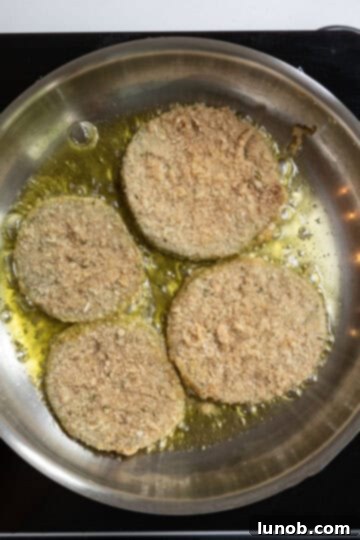 Green tomatoes frying in hot olive oil in a sauté pan, turning golden brown.