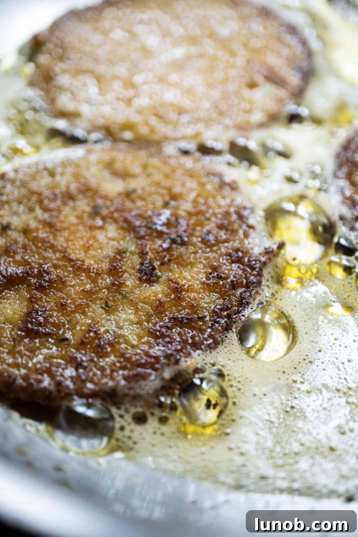 Multiple slices of green tomatoes frying in olive oil in a pan, achieving a perfect golden crisp.