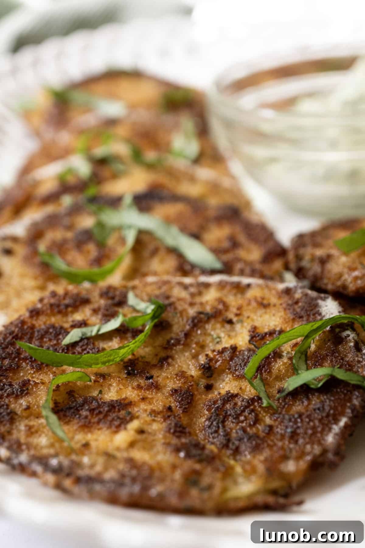 A close-up of crispy Italian Fried Green Tomatoes served with a bowl of garlic basil aioli, garnished with fresh basil leaves.